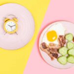 un piatto con dentro del cibo e un altro con dentro una sveglia come simbolo della dieta intermittente