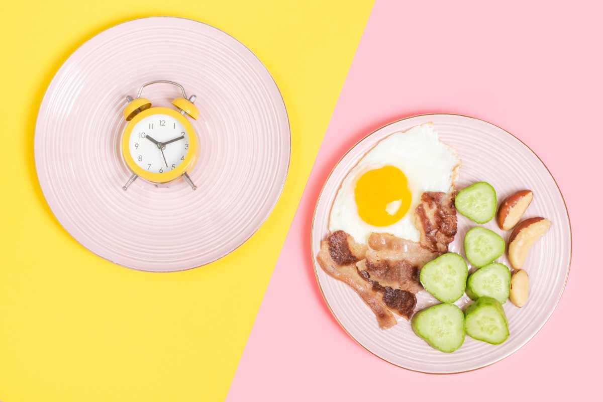 un piatto con dentro del cibo e un altro con dentro una sveglia come simbolo della dieta intermittente